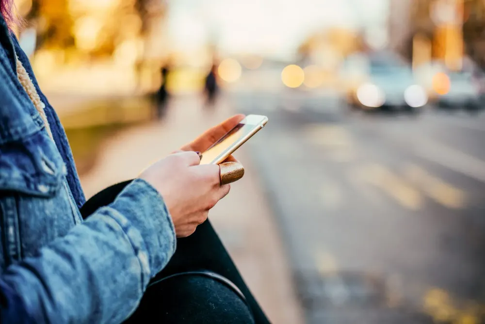 Close-up on hands of person using smartphone next to a busy street